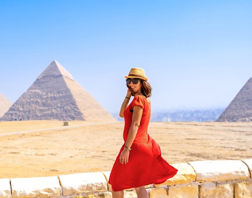 Tourist in red dress posing in front of Pyramids of Giza, Egypt.