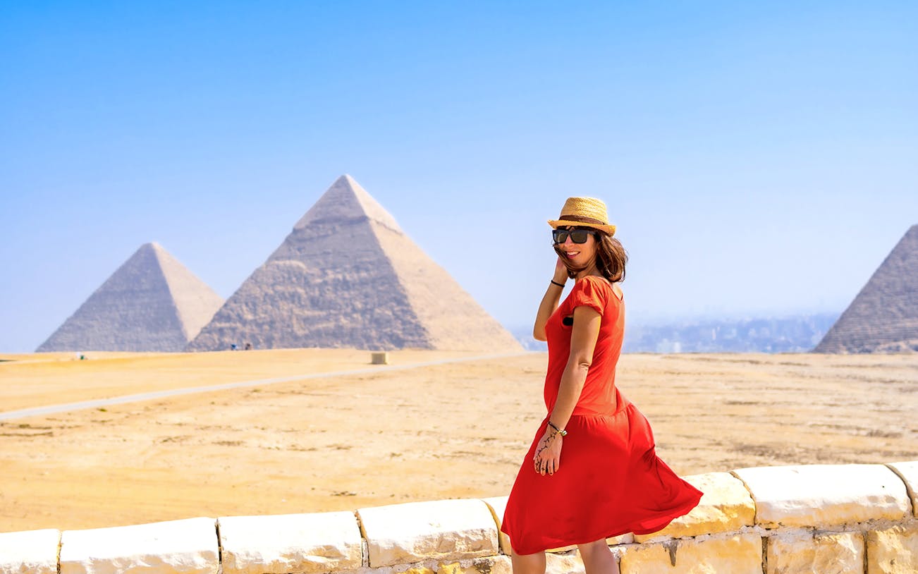 Tourist in red dress posing in front of Pyramids of Giza, Egypt.