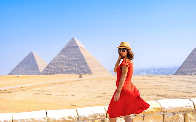 Tourist in red dress posing in front of Pyramids of Giza, Egypt.