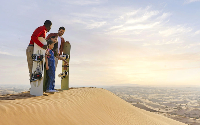 Guide with family holding sandboards on desert dune.