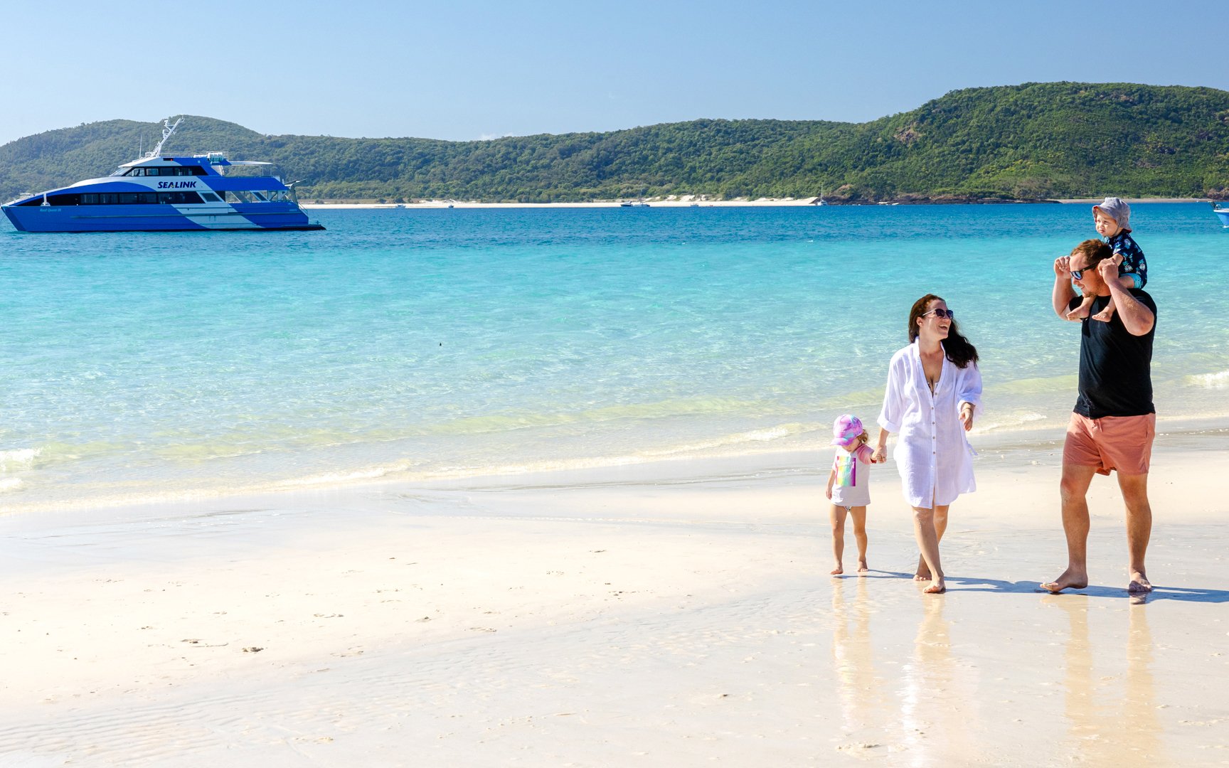 Family walking on Whitehaven Beach with a boat in the background, Airlie Beach tour.