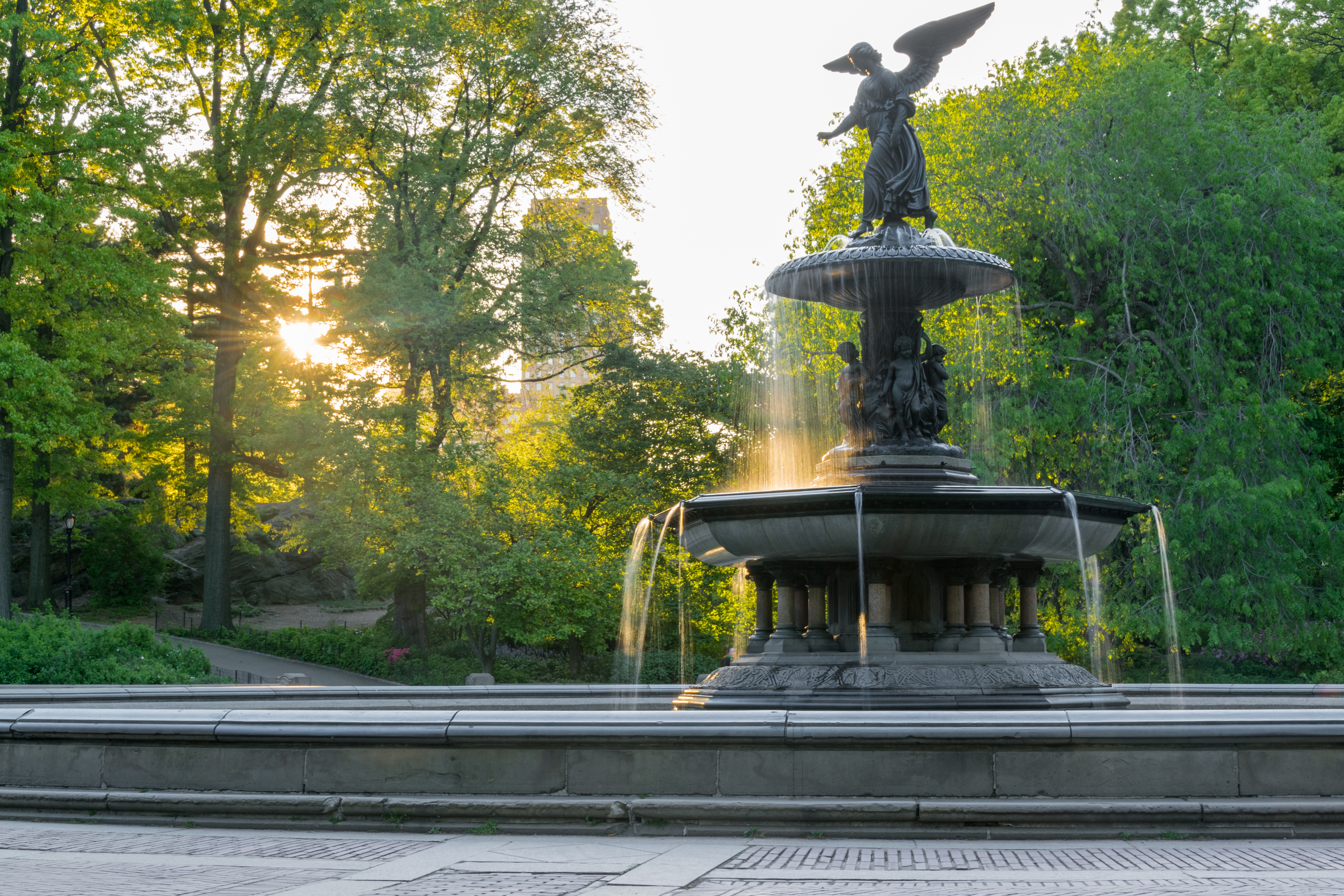 Bethesda Terrace and Fountain in Central Park with sunlight filtering through trees.