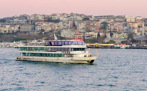 Sightseeing cruise ship on the Bosphorus Strait with Istanbul cityscape in the background.