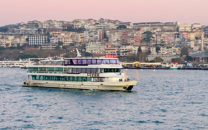 Sightseeing cruise ship on the Bosphorus Strait with Istanbul cityscape in the background.
