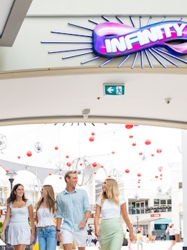 Group walking under Infinity Attraction sign at Gold Coast shopping center.