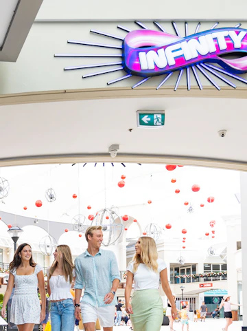 Group walking under Infinity Attraction sign at Gold Coast shopping center.
