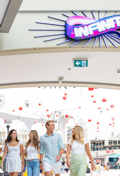 Group walking under Infinity Attraction sign at Gold Coast shopping center.