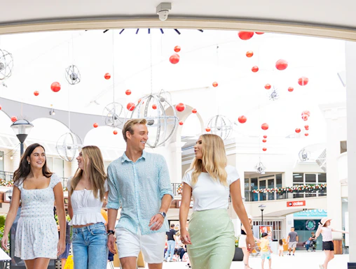 Group walking under Infinity Attraction sign at Gold Coast shopping center.