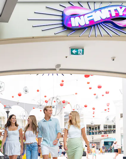Group walking under Infinity Attraction sign at Gold Coast shopping center.