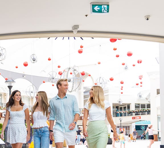 Group walking under Infinity Attraction sign at Gold Coast shopping center.