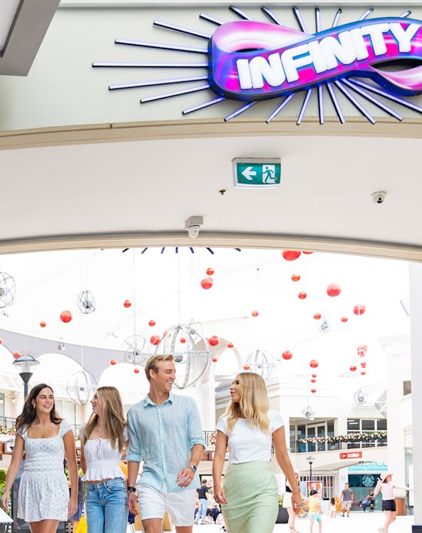 Group walking under Infinity Attraction sign at Gold Coast shopping center.