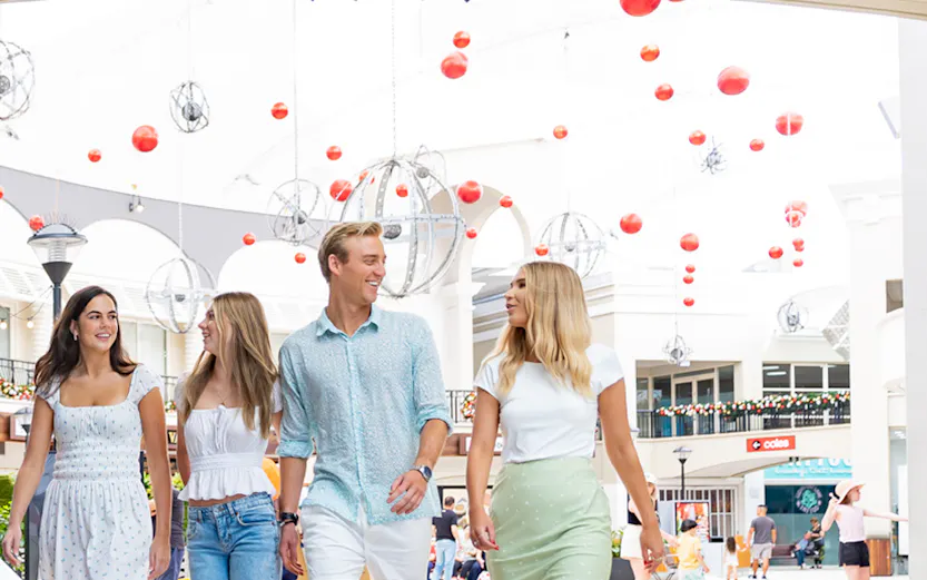 Group walking under Infinity Attraction sign at Gold Coast shopping center.
