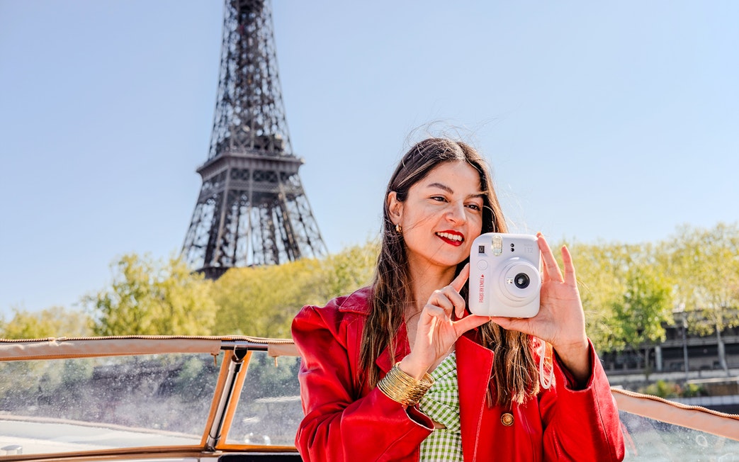 Person taking a Polaroid on Seine cruise with Eiffel Tower in background.