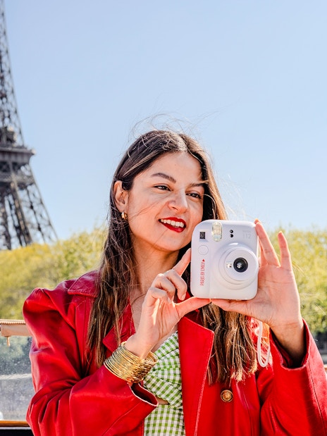 Person taking a Polaroid on Seine cruise with Eiffel Tower in background.