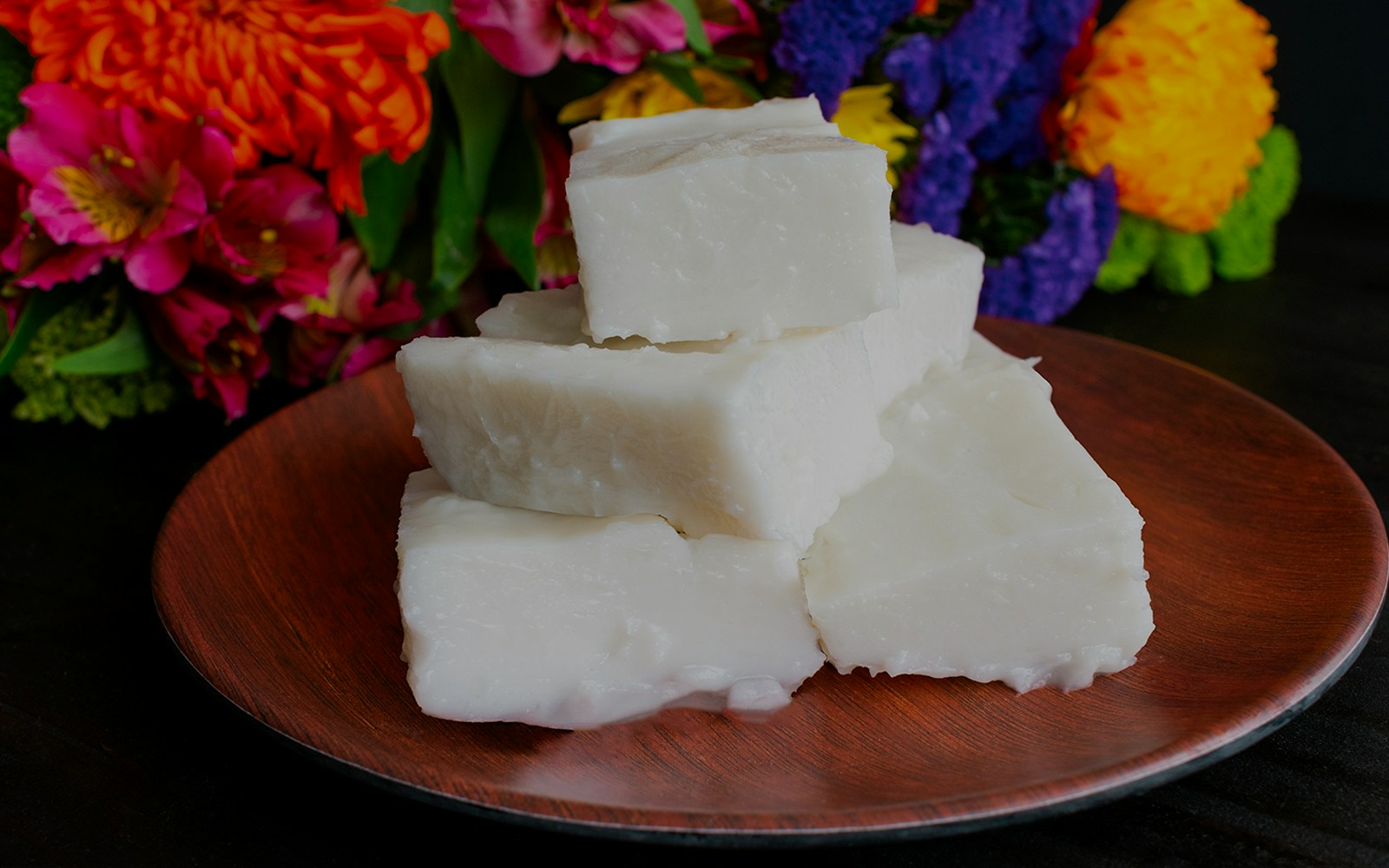 Haupia coconut pudding squares on a wooden plate with colorful flowers in the background.