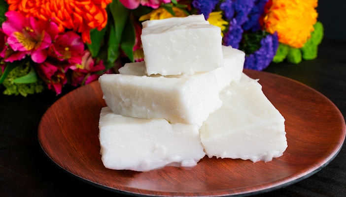 Haupia coconut pudding squares on a wooden plate with colorful flowers in the background.