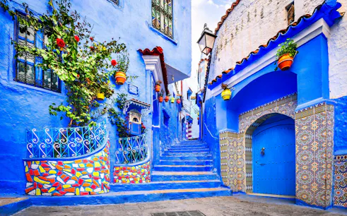Narrow blue alley with colorful pots and mosaic tiles in Chefchaouen, Morocco.