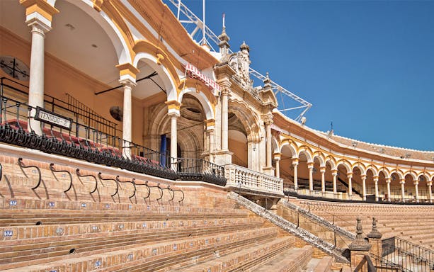 Seville bullring arena with arched seating and ornate architecture.