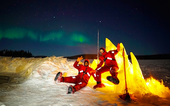 Two people in red suits enjoying Northern Lights ice floating experience.