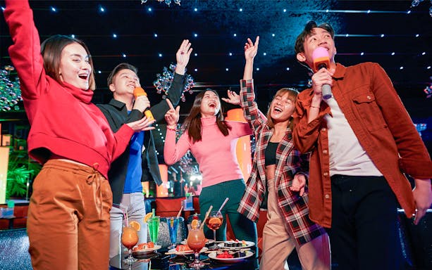 Group enjoying karaoke and drinks at a vibrant indoor venue in Singapore.