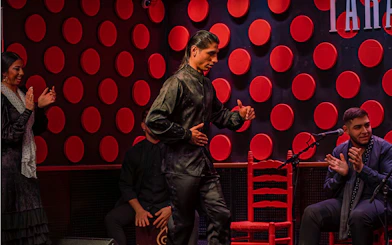 Flamenco dancer performing at Los Tarantos show in Barcelona with musicians clapping.