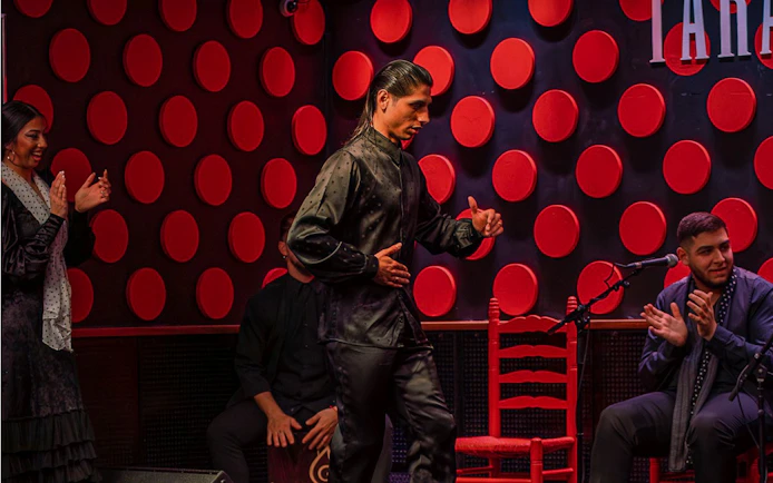 Flamenco dancer performing at Los Tarantos show in Barcelona with musicians clapping.