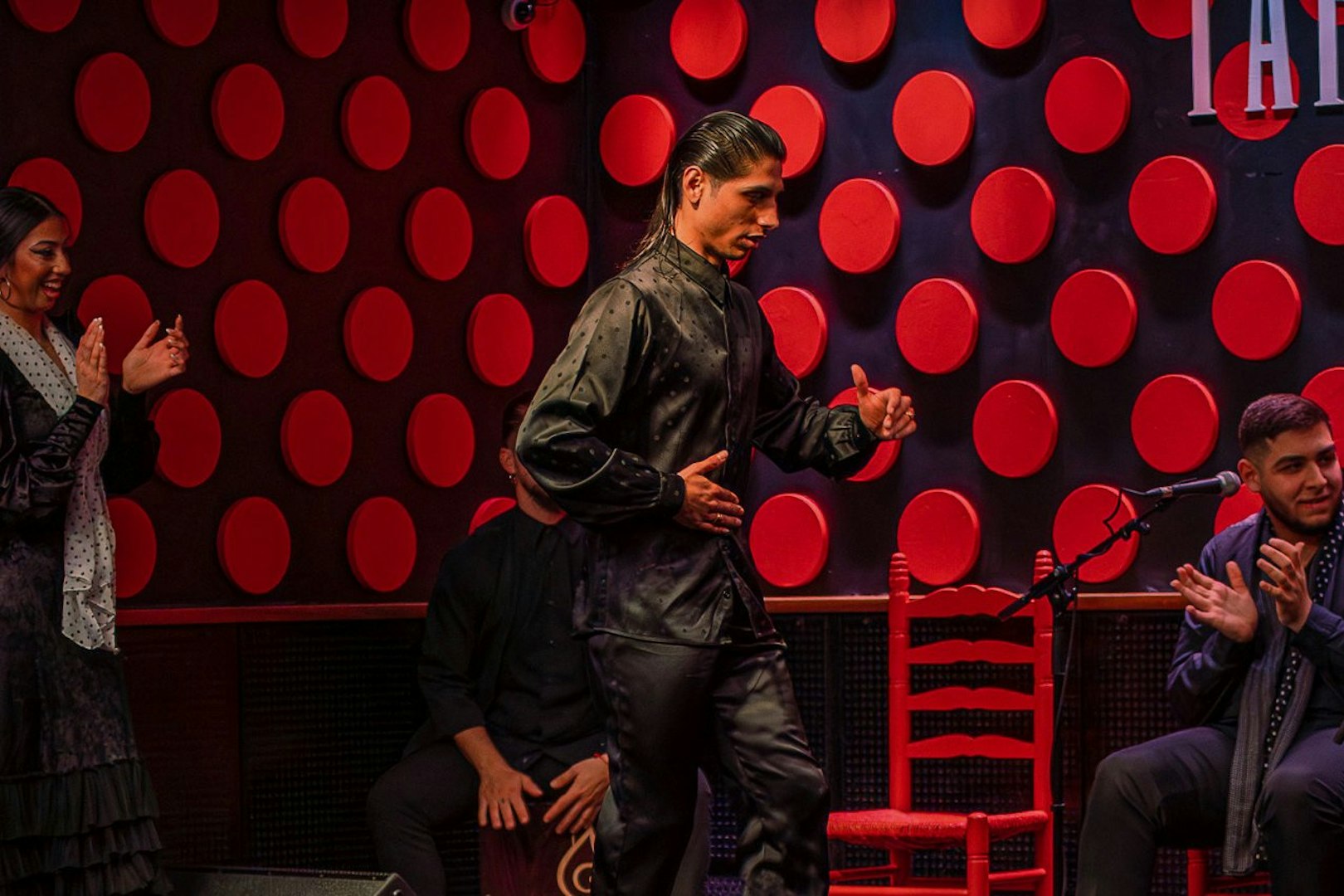 Flamenco dancer performing at Los Tarantos show in Barcelona with musicians clapping.