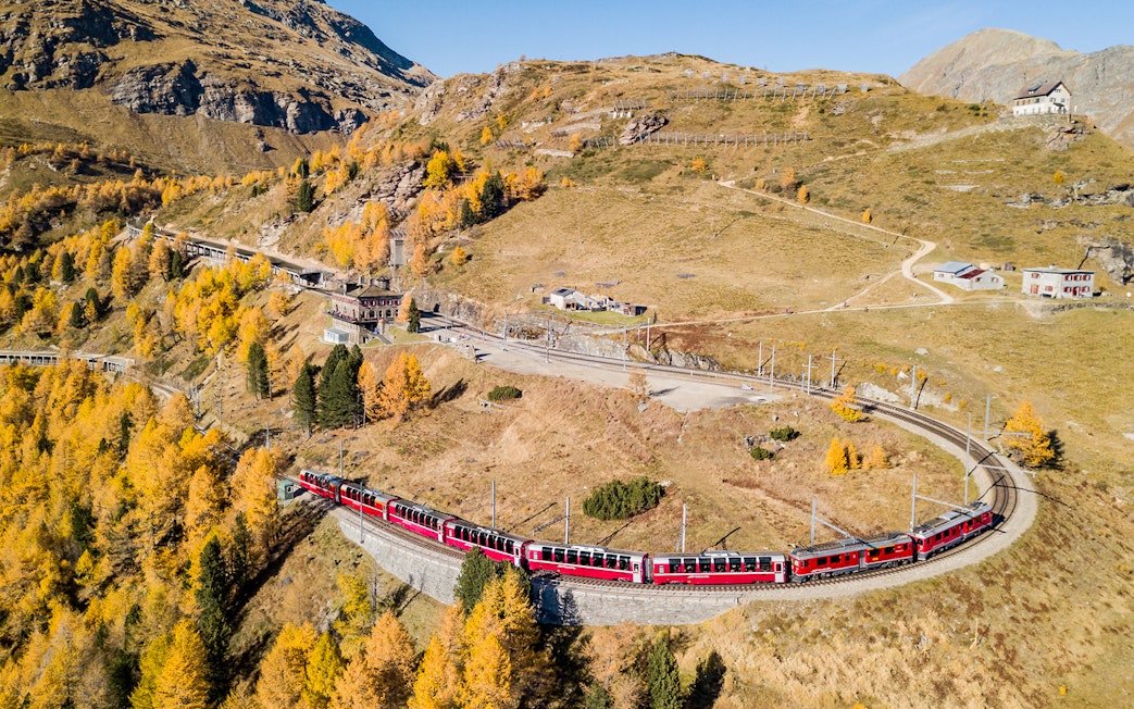 Mountain train on curved track at Jungfraujoch railway station amidst autumn landscape.