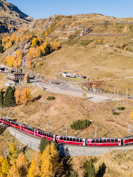 Mountain train on curved track at Jungfraujoch railway station amidst autumn landscape.