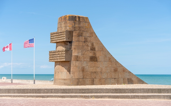 Normandy D-Day monument with Canadian and American flags by the beach.
