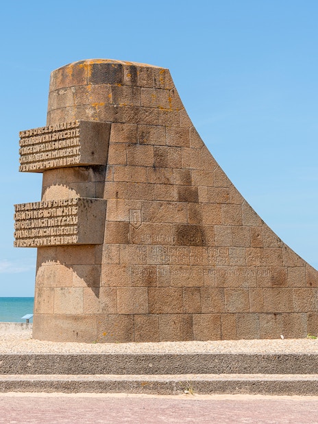Normandy D-Day monument with Canadian and American flags by the beach.