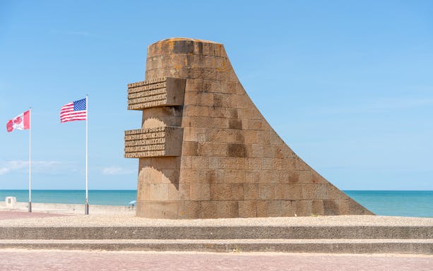 Normandy D-Day monument with Canadian and American flags by the beach.