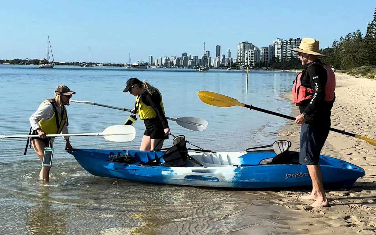 Kayakers preparing to launch on Gold Coast guided tour with city skyline in background.