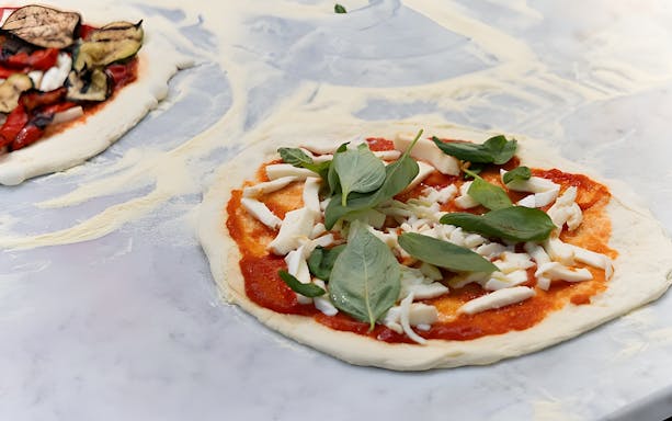 Participants making pizza and tiramisu in a Rome kitchen cooking class.