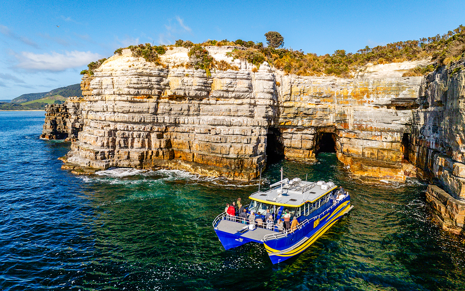 Boat tour near Tasman Peninsula cliffs, Cape Raoul, with rocky formations and clear blue water.