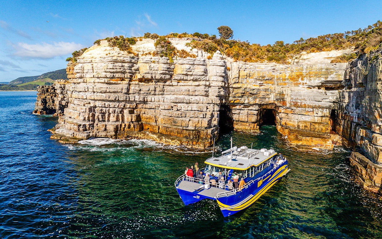 Boat tour near Tasman Peninsula cliffs, Cape Raoul, with rocky formations and clear blue water.