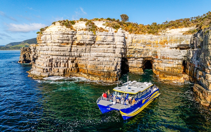Boat tour near Tasman Peninsula cliffs, Cape Raoul, with rocky formations and clear blue water.