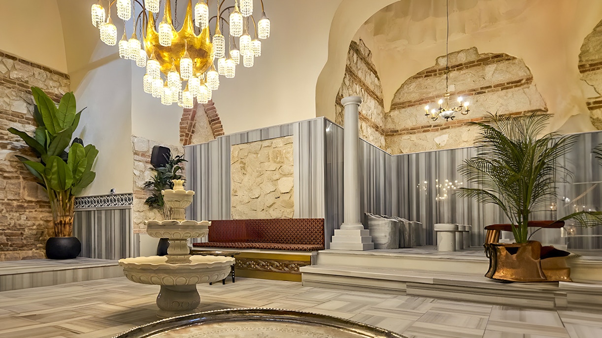 Gedikpasa Historical Hammam interior with marble fountain and ornate chandelier.