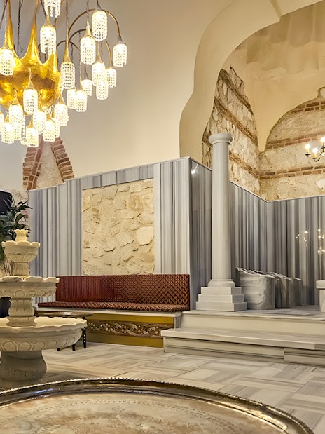 Gedikpasa Historical Hammam interior with marble fountain and ornate chandelier.