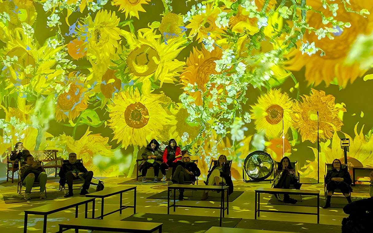 Guests seated at Van Gogh exhibition in London with sunflower projections.