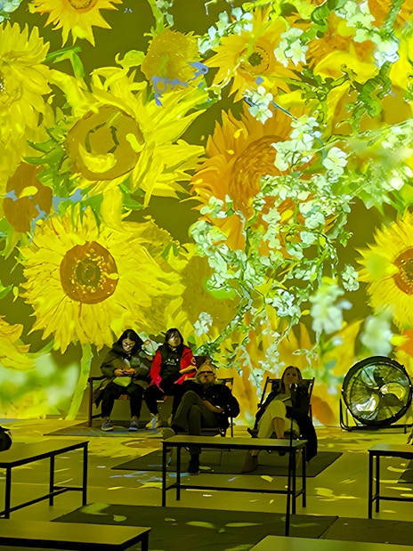 Guests seated at Van Gogh exhibition in London with sunflower projections.