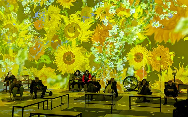 Guests seated at Van Gogh exhibition in London with sunflower projections.