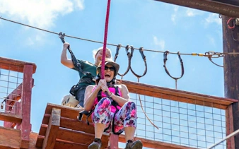 Participant on zip line at Adventure Course Extreme with climbing wall and freefall.