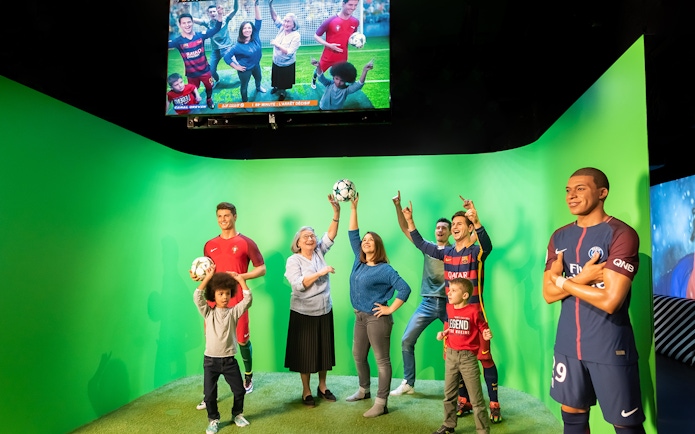 Statues of Lionel Messi and Kylian Mbappe at Grévin Paris wax museum with visitors.