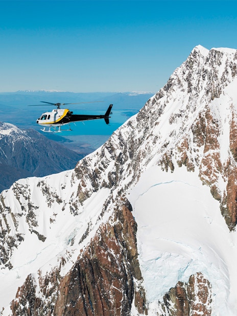 Helicopter flying over snow-covered peaks near Fox Glacier, New Zealand.