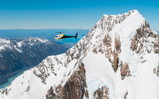 Helicopter flying over snow-covered peaks near Fox Glacier, New Zealand.