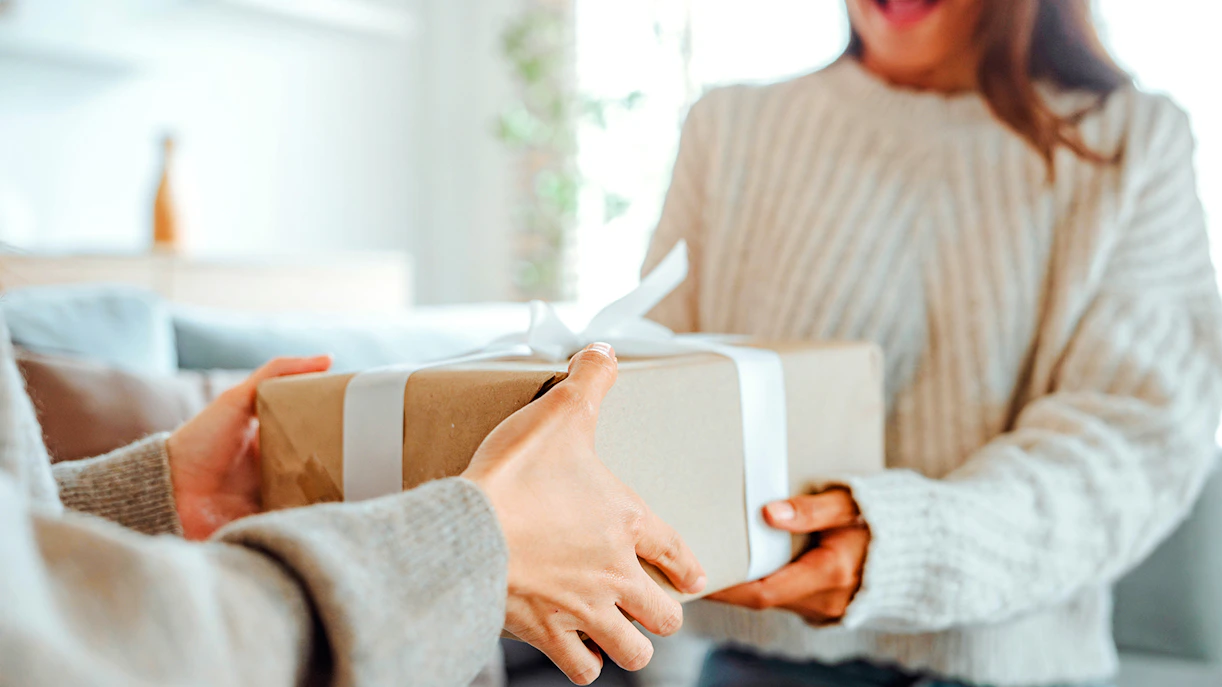 Woman receiving a surprise gift box with a white ribbon indoors.