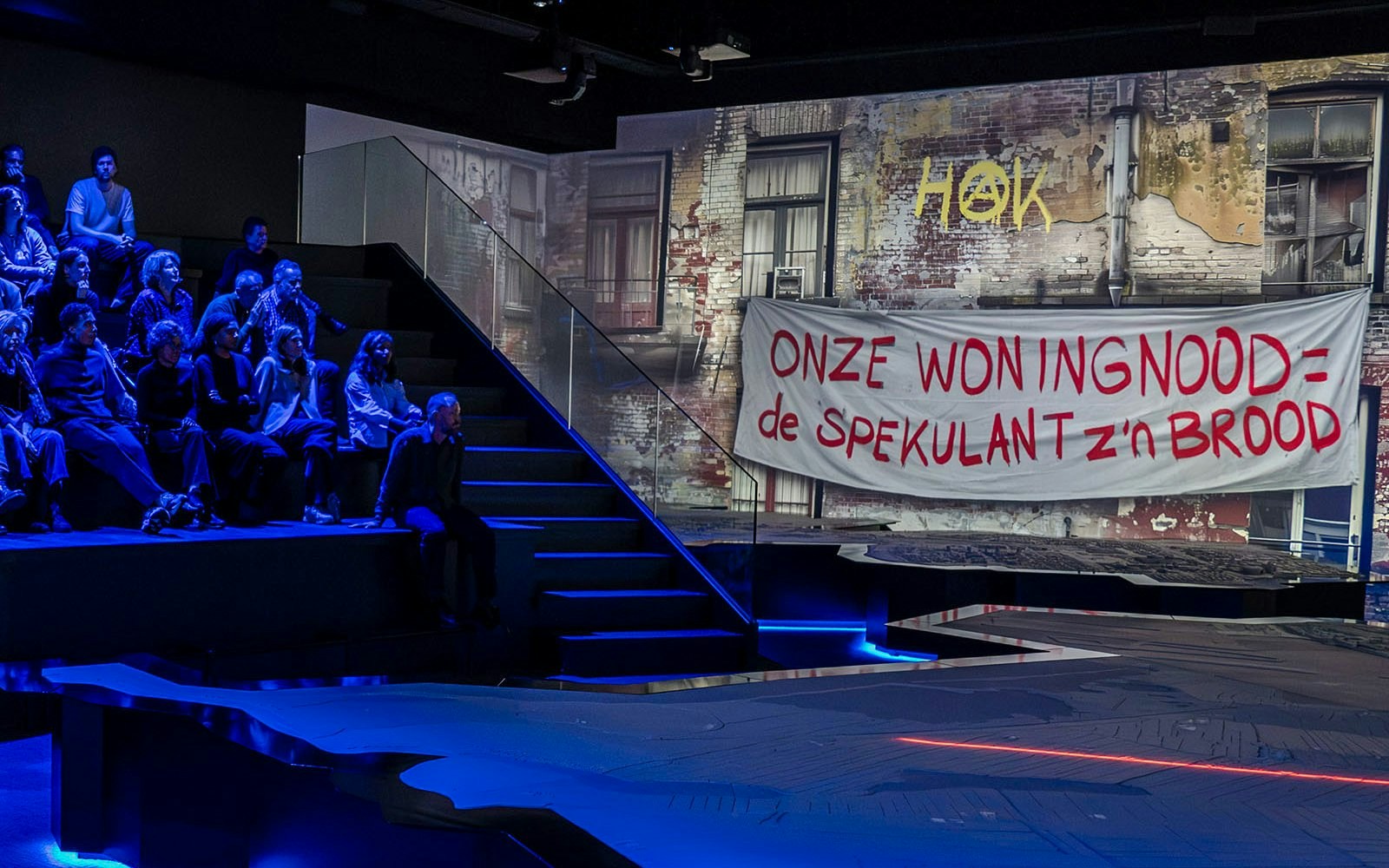 Audience watching a performance at the Amsterdam in Motion exhibit with a protest banner displayed.