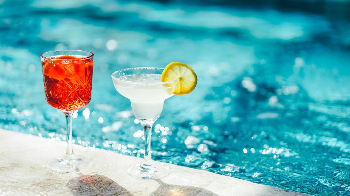 Cocktails by the poolside with a vibrant blue water backdrop.