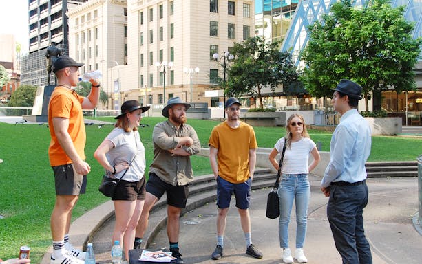 Group of tourists listening to a guide in a Brisbane park during a walking tour.